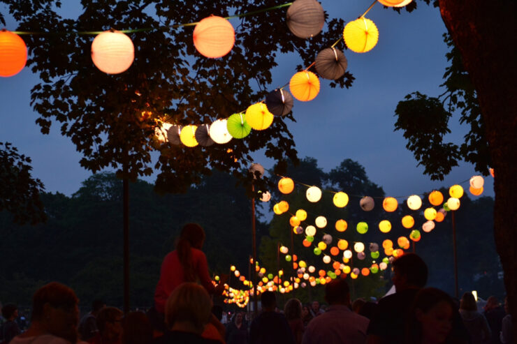 Verschiedenfarbige Lampions vor dunklem Himmel im Westfalenpark, im unteren Bildteil sind viele Menschen, ein Kind wird Huckepack getragen Bild: Stadt Dortmund/Stefanie Kleemann