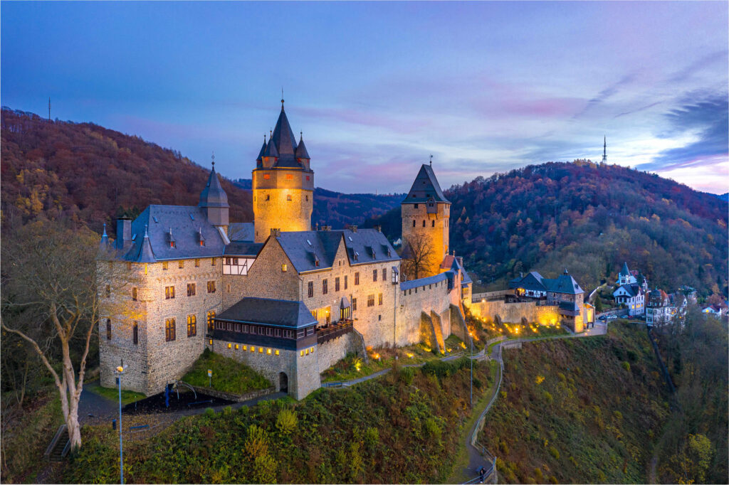 Zentralperspektive der Burg Altena umgeben von einer bergigen Landschaft: Die helle Beleuchtung versetzt das Schloss in eine magische Atmosphäre.
(Foto: Andreas Giesbrecht-Mantler)